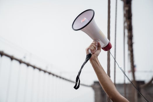 A hand holding a megaphone, symbolizing protest or announcement at an outdoor rally.